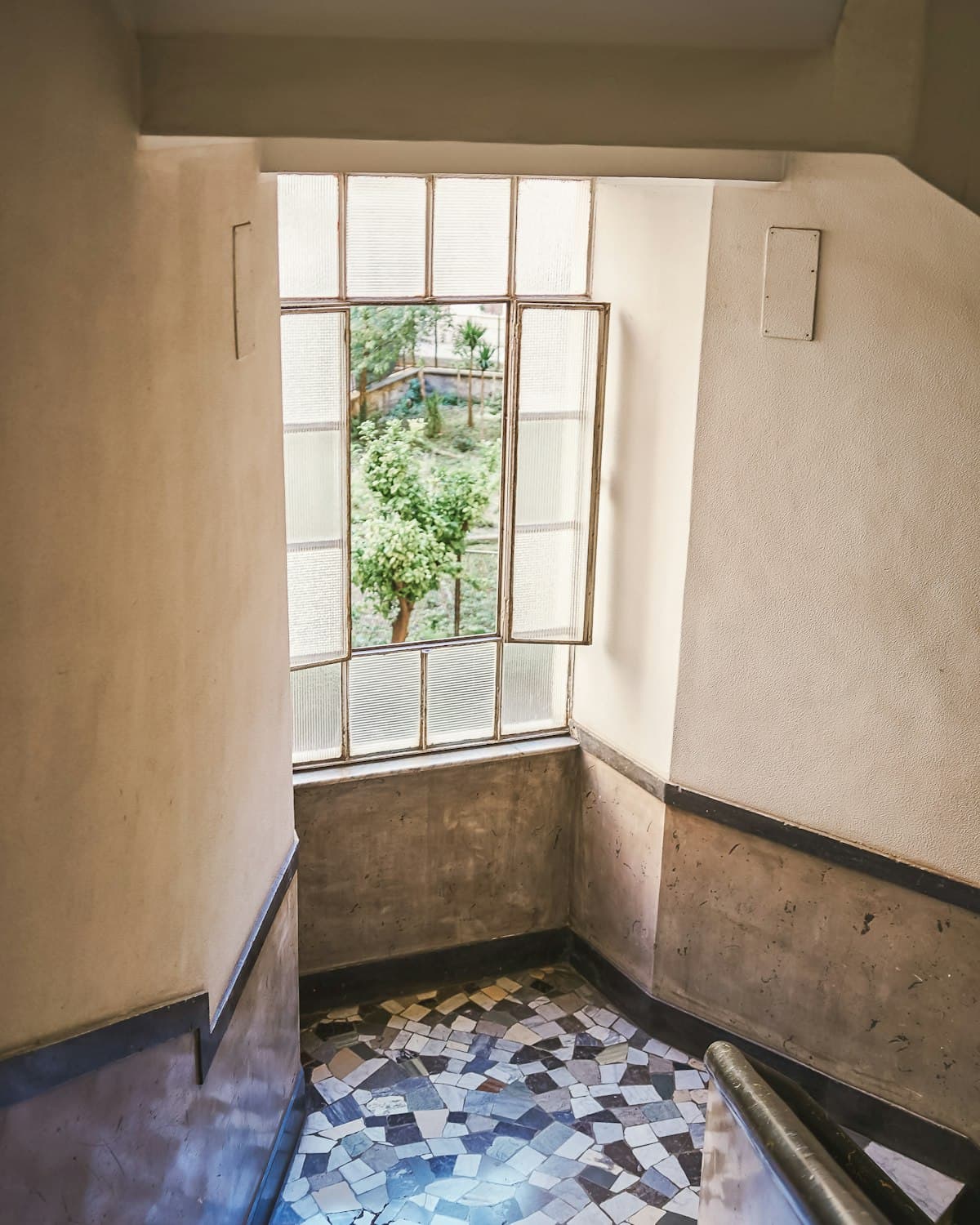 Treppenabsatz eines Altbaus mit Sprossenfenster und Mosaikfliesenboden