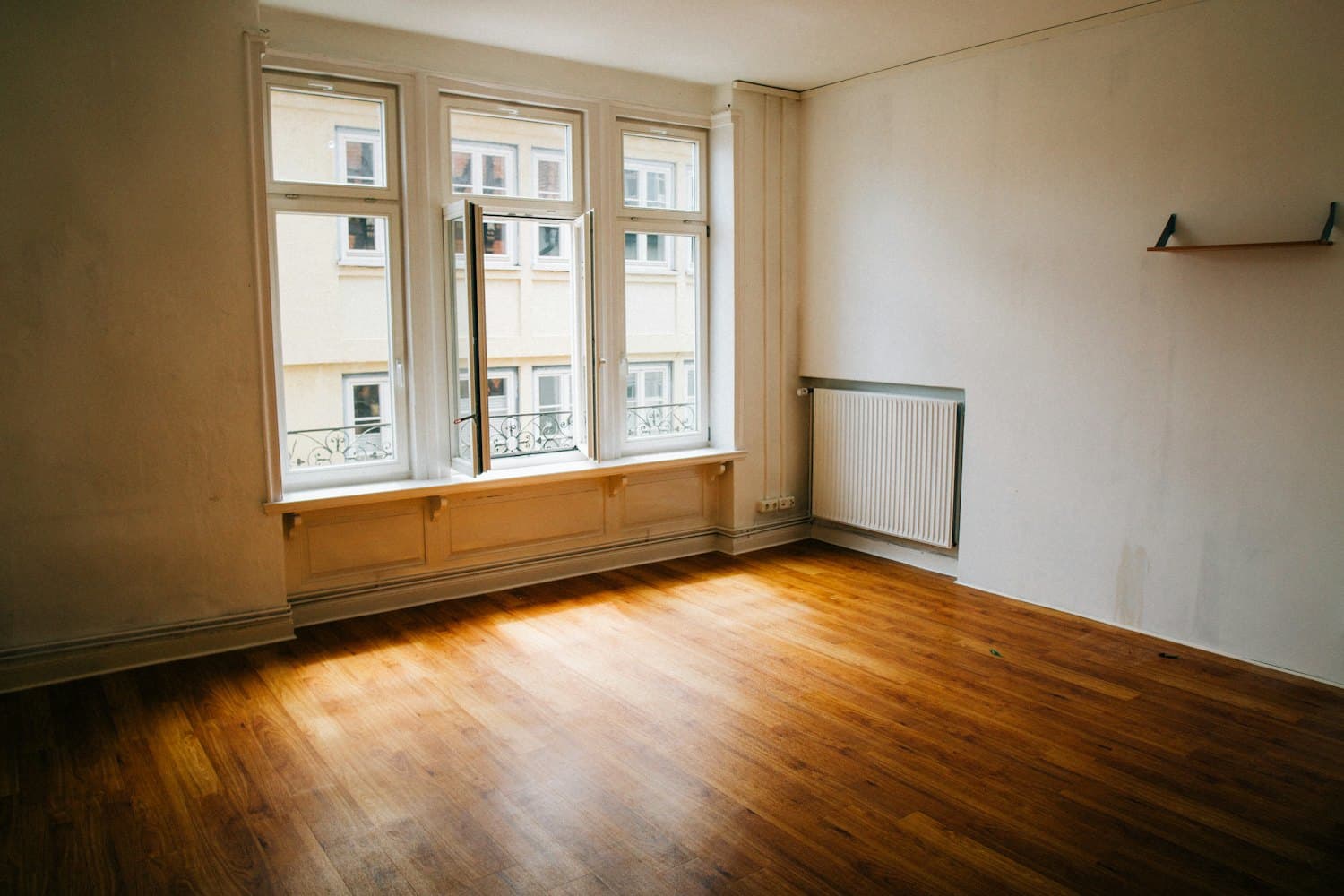 Leere Altbauwohnung mit Dielenboden, Sprossenfenstern und Heizkörper unter der Fensterbank